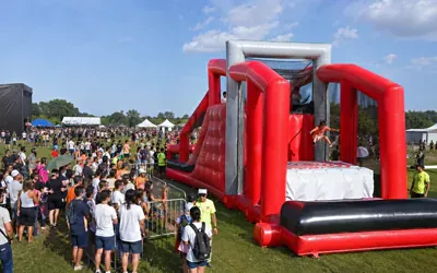 Juego inflable rojo de gran tamaño con una larga fila de asistentes en un festival masivo al aire libre.